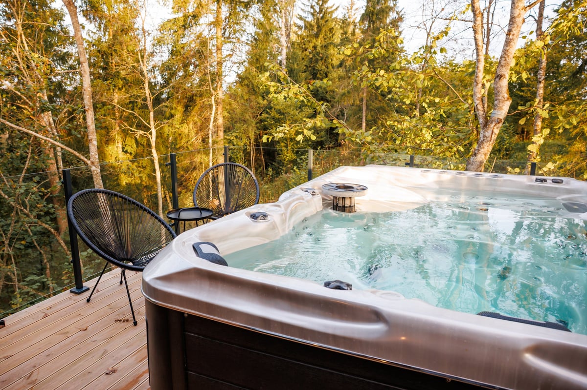 A modern hot tub on a wooden deck surrounded by tall trees with warm lighting in a premium setting