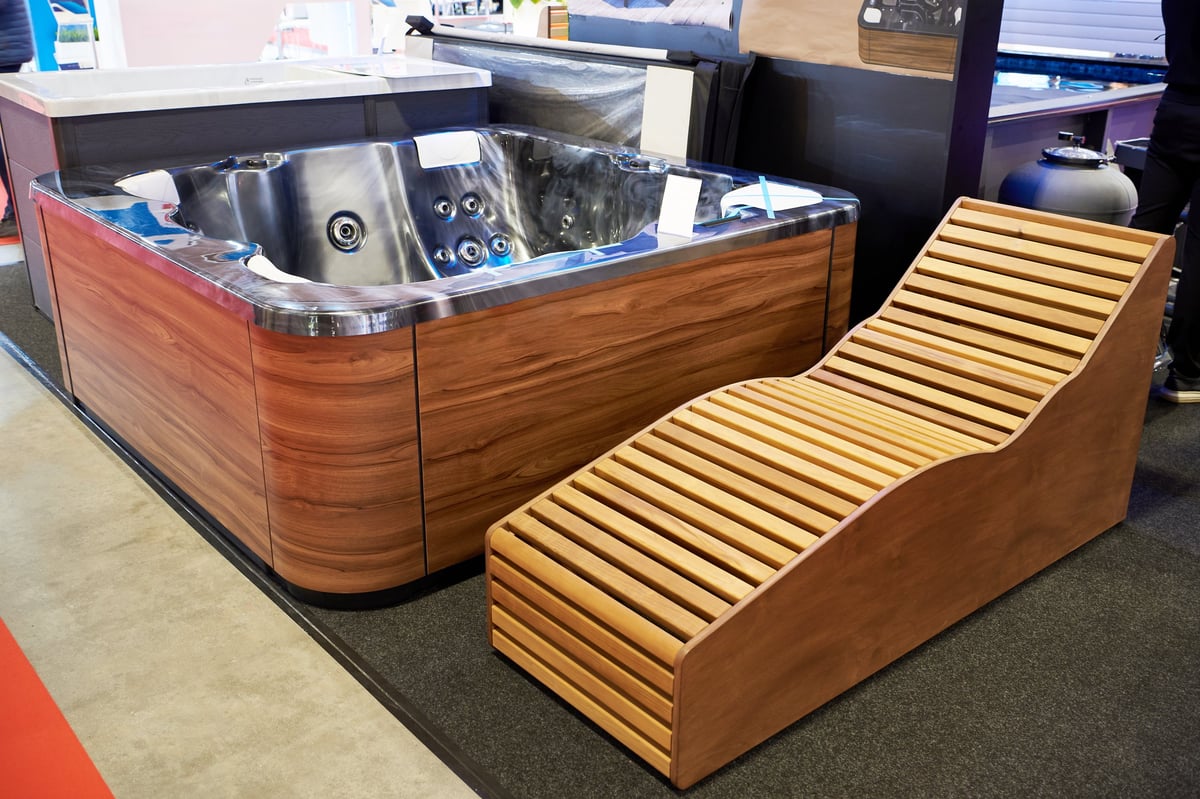 Modern outdoor hot tub with integrated jets and wooden lounge chair displayed in a showroom